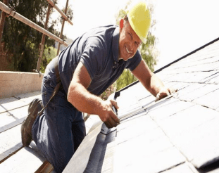 A man in blue shirt and yellow hard hat working on roof.